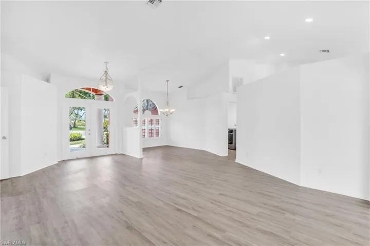 Unfurnished living room featuring high vaulted ceiling, a chandelier, light hardwood / wood-style floors, and french doors