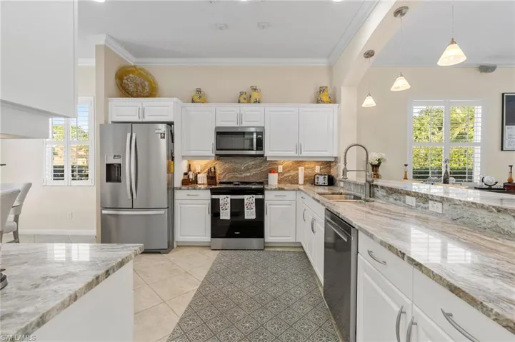 Kitchen featuring light stone counters, white cabinets, ornamental molding, and plenty of natural light