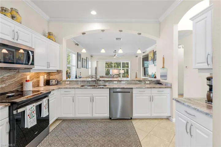 Kitchen with white cabinetry, appliances with stainless steel finishes, ornamental molding, backsplash, and pendant lighting