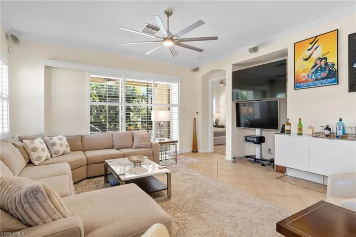 Living room featuring ornamental molding, arched walkways, a ceiling fan, and light tile patterned floors
