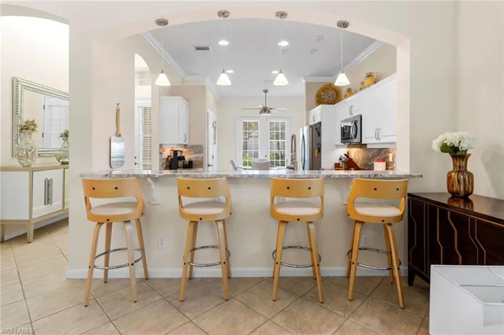 Kitchen with tasteful backsplash, a breakfast bar area, white cabinetry, hanging light fixtures, and ornamental molding