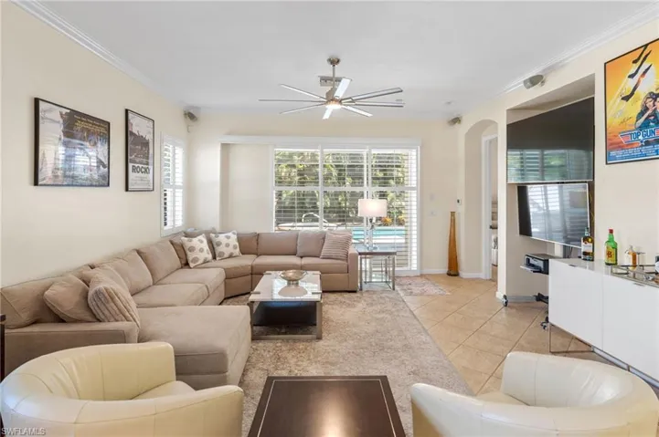 Living area featuring crown molding, plenty of natural light, light tile patterned flooring, a ceiling fan, and arched walkways