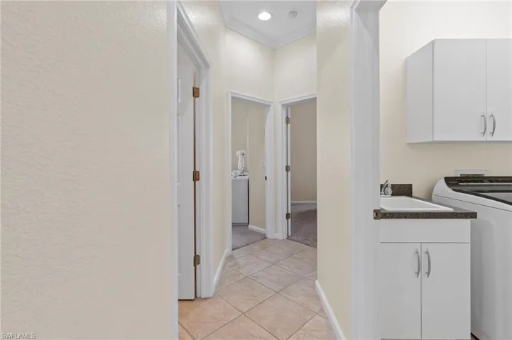 Washroom featuring washer / dryer, ornamental molding, cabinet space, light tile patterned flooring, and a textured wall