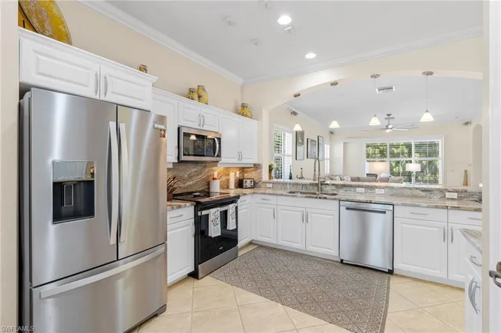 Kitchen with appliances with stainless steel finishes, white cabinets, ornamental molding, hanging light fixtures, and backsplash