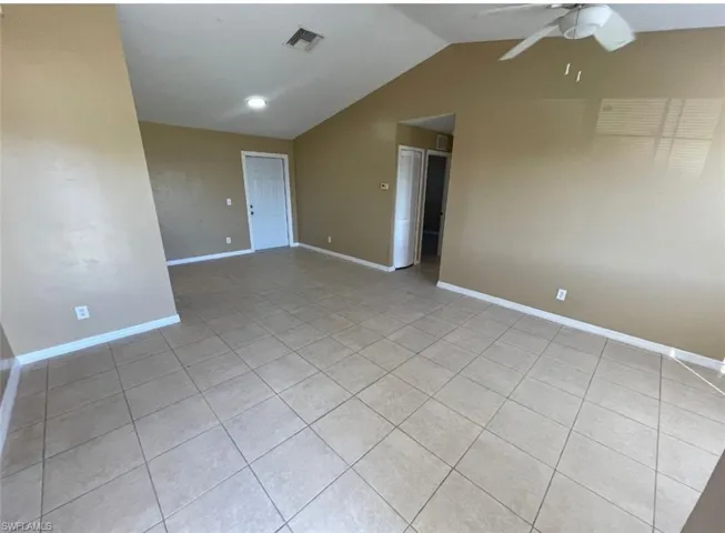 Empty room featuring light tile patterned floors, ceiling fan, baseboards, lofted ceiling, and visible vents
