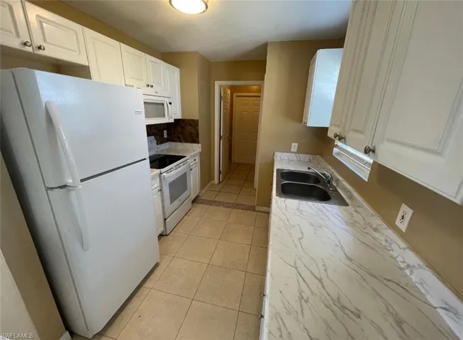 Kitchen featuring a sink, decorative backsplash, light tile patterned flooring, white appliances, and white cabinets