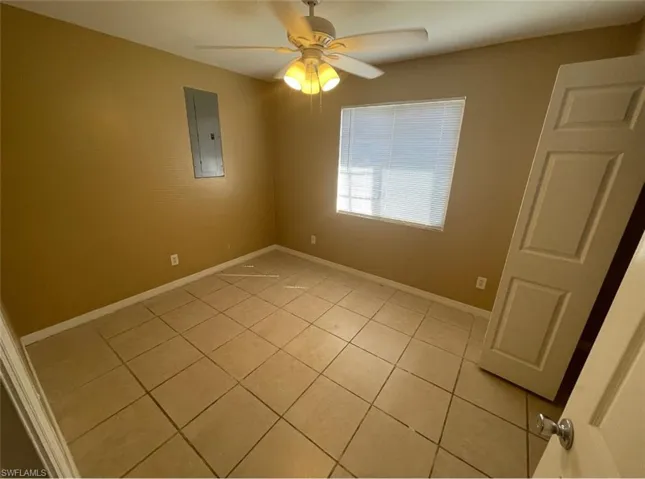 Empty room with electric panel, a ceiling fan, baseboards, and light tile patterned floors
