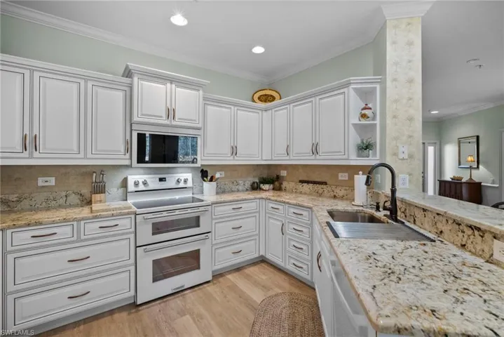 Kitchen with range with two ovens, open shelves, light stone counters, white cabinets, and ornamental molding