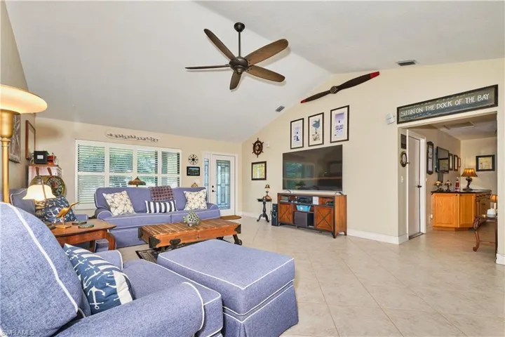 Living area with lofted ceiling, light tile patterned floors, baseboards, visible vents, and ceiling fan