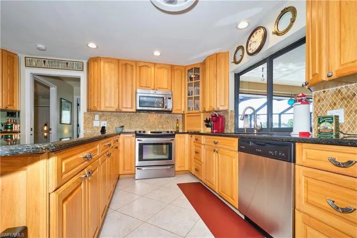 Kitchen featuring light tile patterned floors, dark stone counters, a sink, appliances with stainless steel finishes, and glass insert cabinets