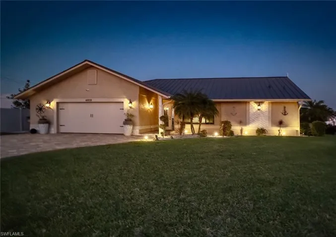 Ranch-style house featuring a garage, stucco siding, a front yard, a standing seam roof, and driveway