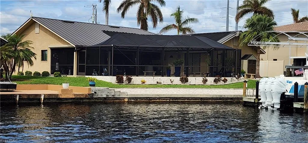 Rear view of house featuring glass enclosure, metal roof, stucco siding, and a water view