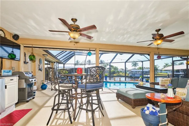 View of patio featuring glass enclosure, grilling area, an outdoor pool, and a ceiling fan