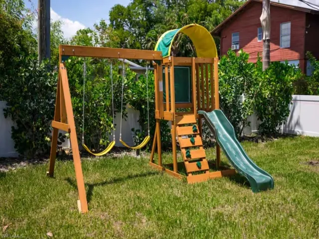 Spacious backyard featuring a wooden playset with two swings, a slide, and climbing steps