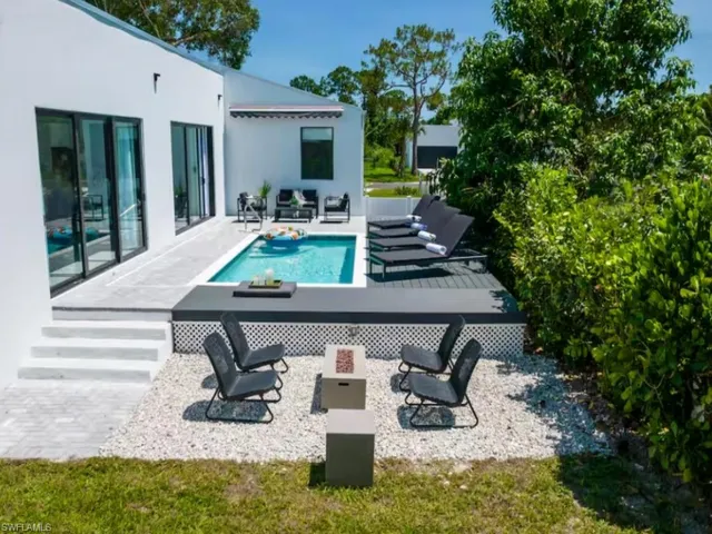 Modern exterior featuring a rectangular swimming pool, an elevated deck, sliding glass door, a white facade, and a white gravel patio with a fireplace