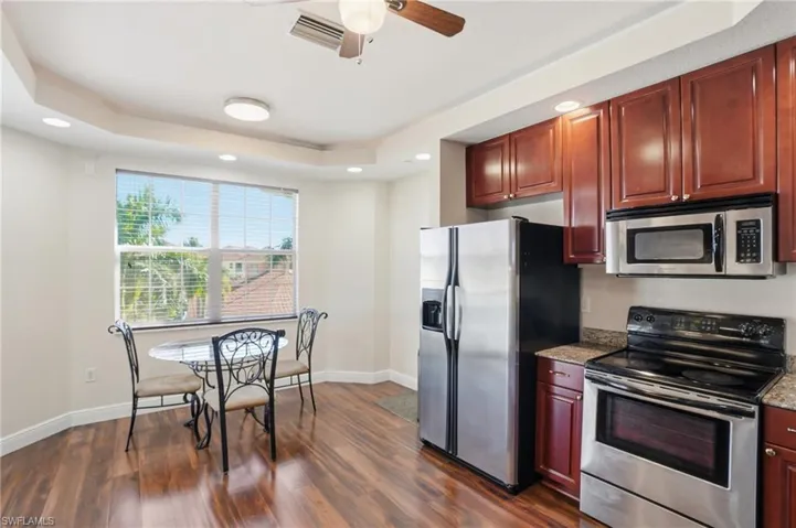 Kitchen with stainless steel appliances, ceiling fan, light stone counters, recessed lighting, and a tray ceiling