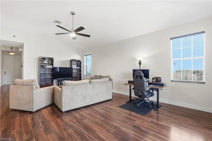 Living area with a desk, vaulted ceiling, dark wood-style floors, and ceiling fan