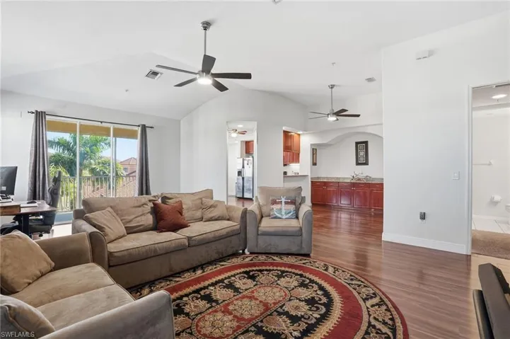 Living area featuring wood finished floors, lofted ceiling, a ceiling fan, and arched walkways