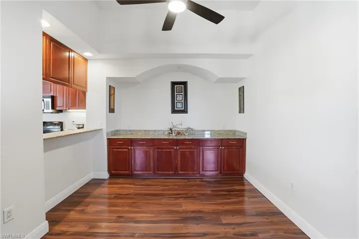 Bar area with bold wood finish cabinets, dark wood-type flooring, light stone countertops, ceiling fan, and range