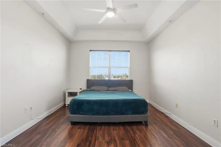 Bedroom with a raised ceiling, dark wood-type flooring, and ceiling fan
