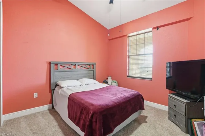 Bedroom with vaulted ceiling, light colored carpet, and a ceiling fan