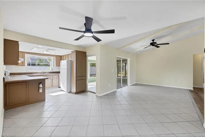 Unfurnished living room with light tile patterned floors, vaulted ceiling, and a ceiling fan