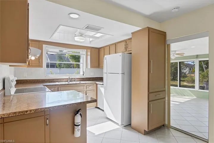 Kitchen featuring white appliances, light tile patterned floors, ceiling fan, a peninsula, and extractor fan