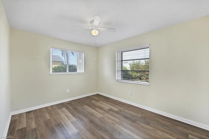Empty room featuring wood finished floors, healthy amount of natural light, a textured ceiling, and a ceiling fan
