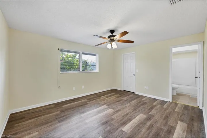 Unfurnished bedroom with a textured ceiling, wood finished floors, a ceiling fan, and connected bathroom