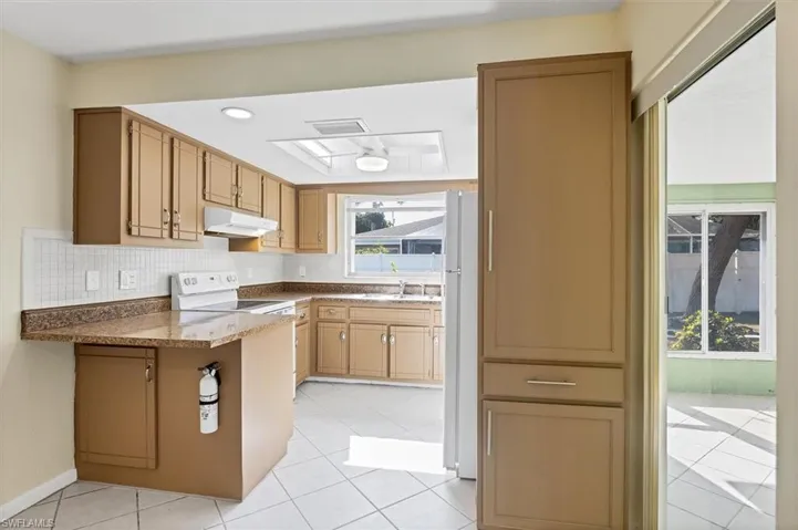 Kitchen with white appliances, a peninsula, backsplash, light tile patterned floors, and recessed lighting