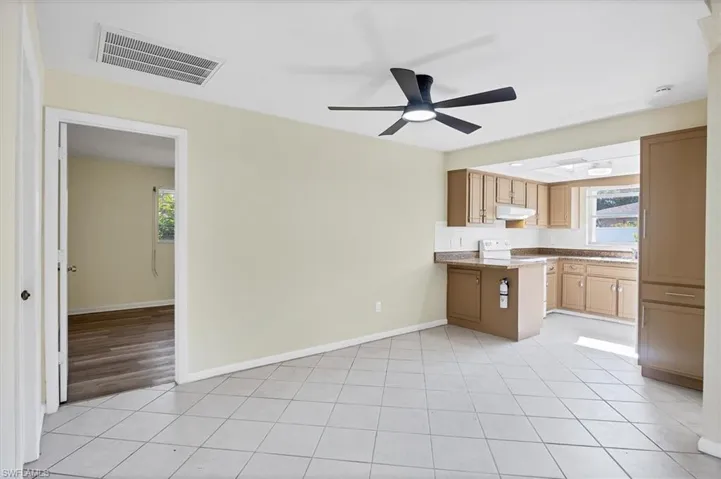 Kitchen featuring a ceiling fan, a peninsula, light tile patterned floors, backsplash, and under cabinet range hood