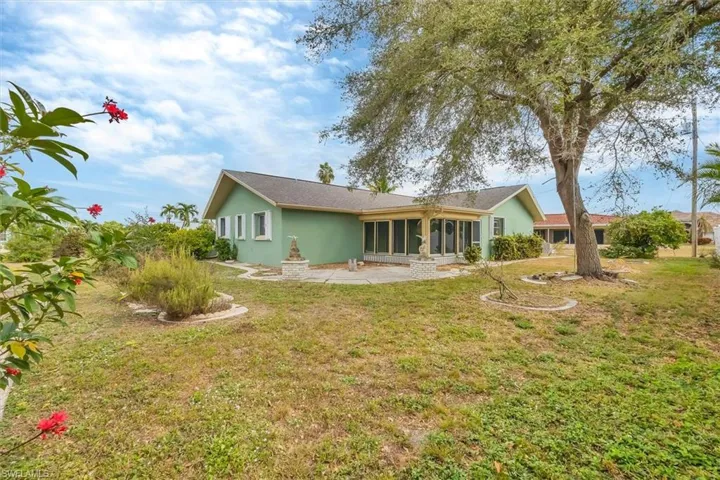 Back of house featuring a patio area, stucco siding, a sunroom, a yard, and roof with shingles