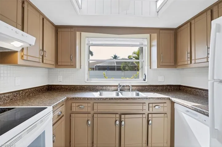 Kitchen with white appliances, dark countertops, under cabinet range hood, and backsplash