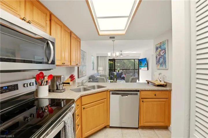 Kitchen featuring stainless steel appliances, open floor plan, light stone countertops, light tile patterned floors, and light wood finish cabinetry