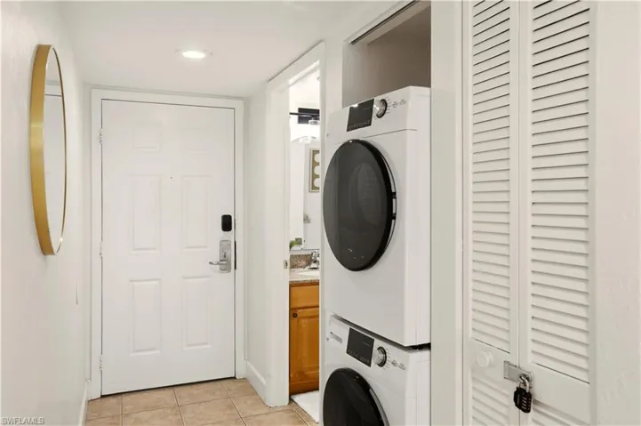 Laundry area featuring light tile patterned flooring, stacked washer / dryer, and recessed lighting