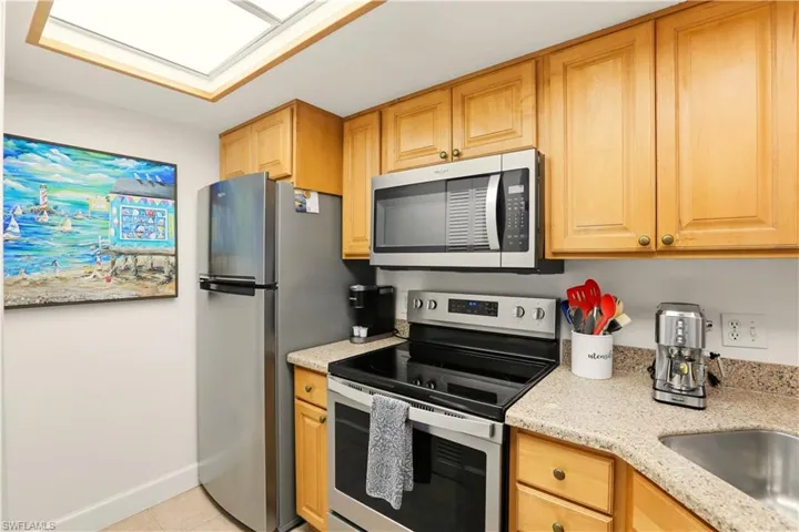 Kitchen featuring stainless steel appliances, light stone countertops, light tile patterned flooring, and a skylight