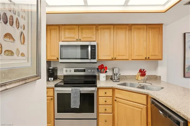 Kitchen featuring stainless steel appliances, light stone counters, and light wood finish cabinetry