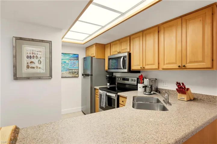 Kitchen featuring stainless steel appliances, light wood finish cabinetry, light stone countertops, and light tile patterned flooring
