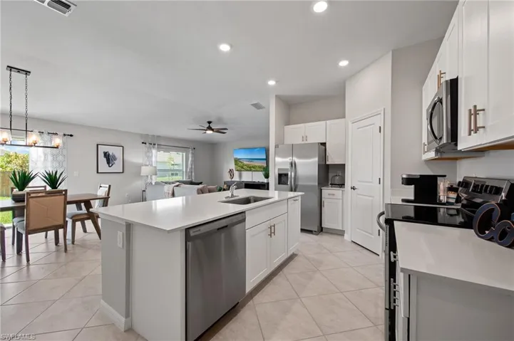 Kitchen with stainless steel appliances, a kitchen island with sink, a ceiling fan, white cabinetry, and recessed lighting