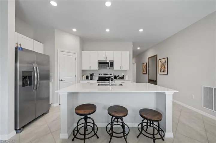 Kitchen featuring stainless steel appliances, light tile patterned flooring, a breakfast bar area, white cabinetry, and a kitchen island with sink