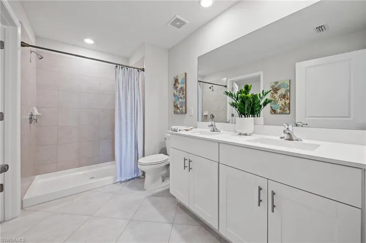 Bathroom featuring double vanity, tile patterned floors, a tile shower, and recessed lighting