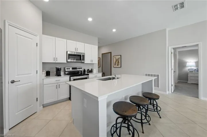 Kitchen with appliances with stainless steel finishes, light tile patterned floors, a kitchen island with sink, a breakfast bar area, and white cabinetry
