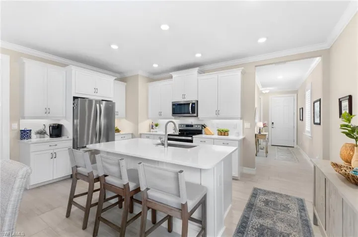 Kitchen with crown molding, sink, a center island with sink, a breakfast bar, and appliances with stainless steel finishes