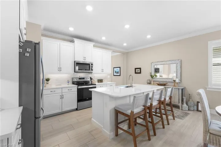 Kitchen featuring decorative backsplash, appliances with stainless steel finishes, a kitchen breakfast bar, and white cabinetry