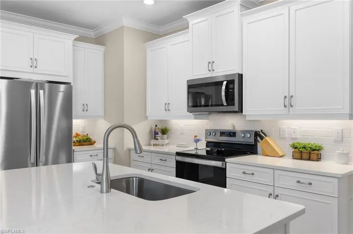 Kitchen with ornamental molding, appliances with stainless steel finishes, white cabinetry, and tasteful backsplash