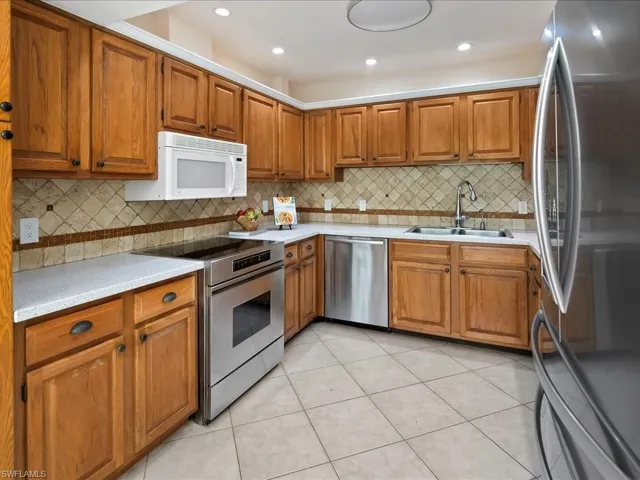 Kitchen featuring stainless steel appliances, brown cabinetry, light tile patterned flooring, backsplash, and recessed lighting