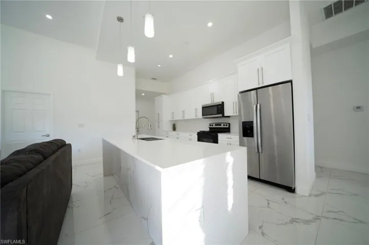 Kitchen with sink, appliances with stainless steel finishes, white cabinetry, hanging light fixtures, and a high ceiling