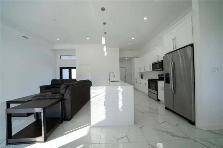 Kitchen featuring sink, appliances with stainless steel finishes, pendant lighting, a kitchen island with sink, and white cabinets