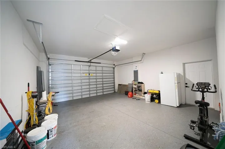 Garage with a garage door opener, electric panel, and white fridge