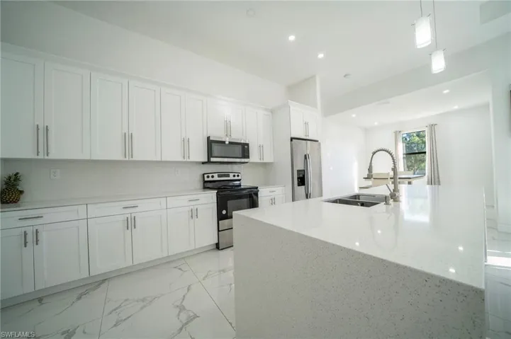 Kitchen with decorative light fixtures, white cabinetry, an island with sink, sink, and stainless steel appliances